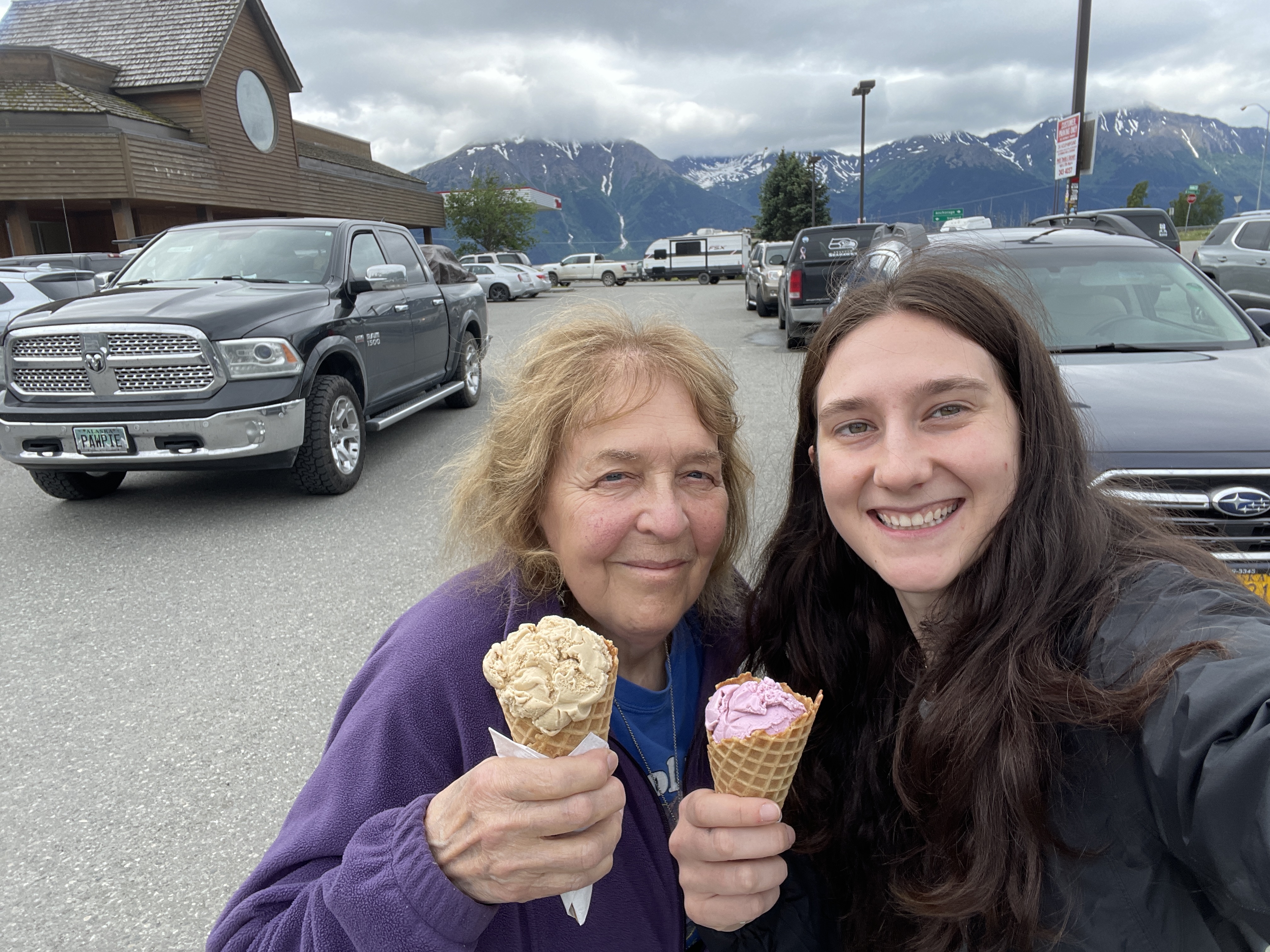 two cuteladies holding ice creams in a parking lot with mountains in the background