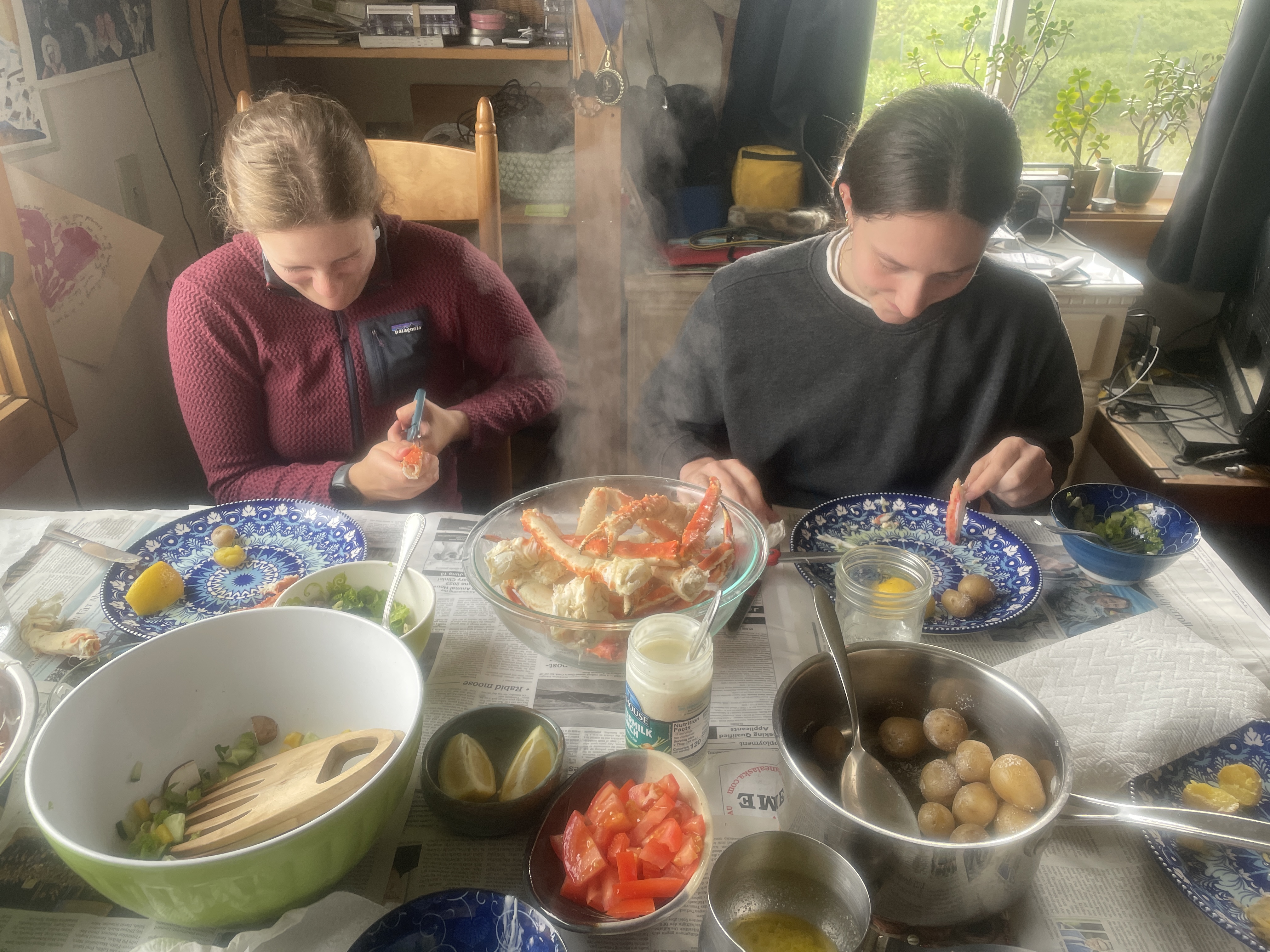 a table with a beautiful bounty of food and two girls sat before it