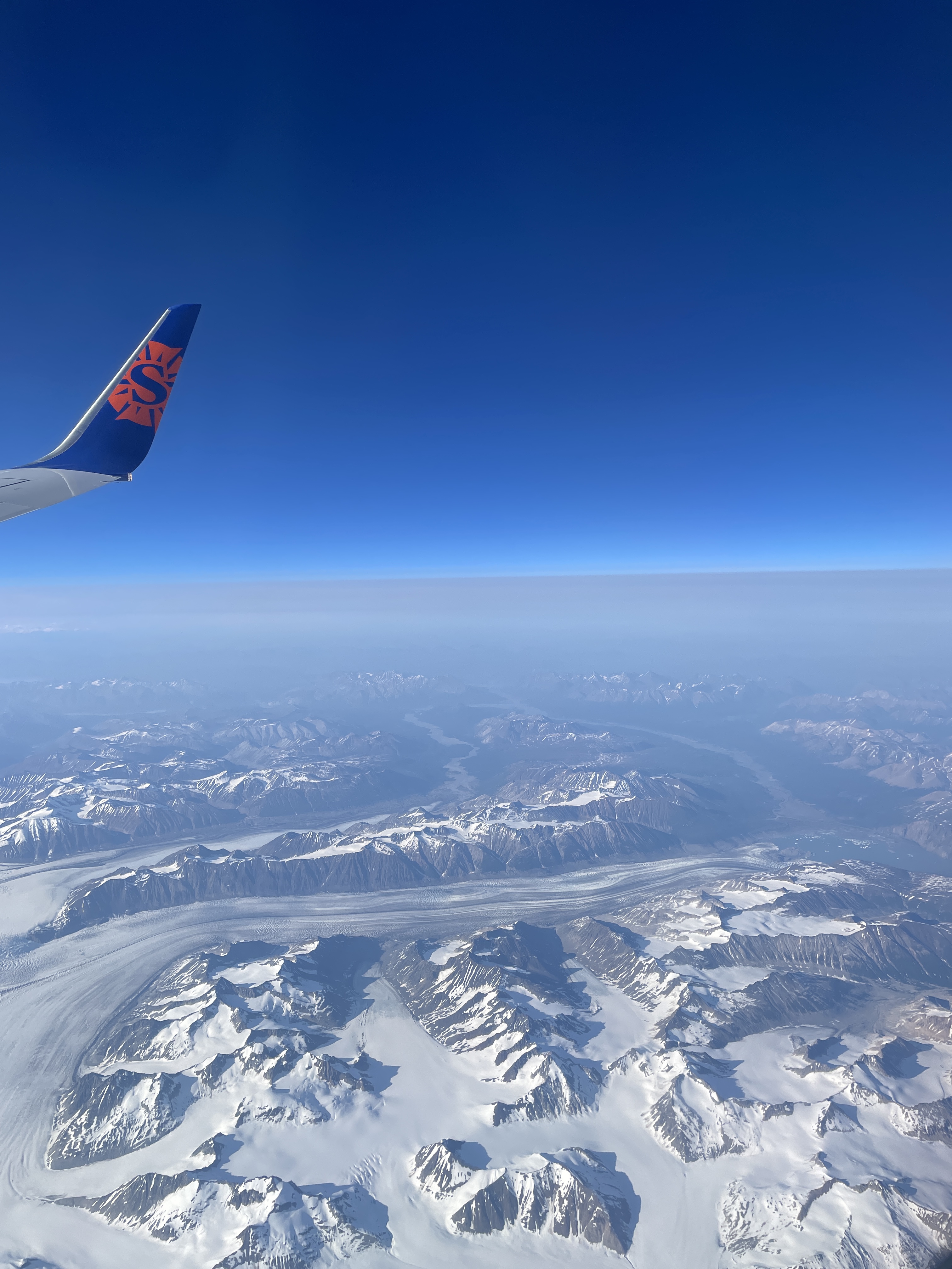 view of a snowy mountain range from a seat on a plane
